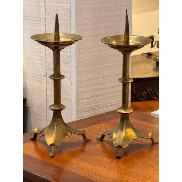 A pair of brass altar pricket sticks with tall, tapering columns and petal-shaped tripod bases. The drip pans feature...