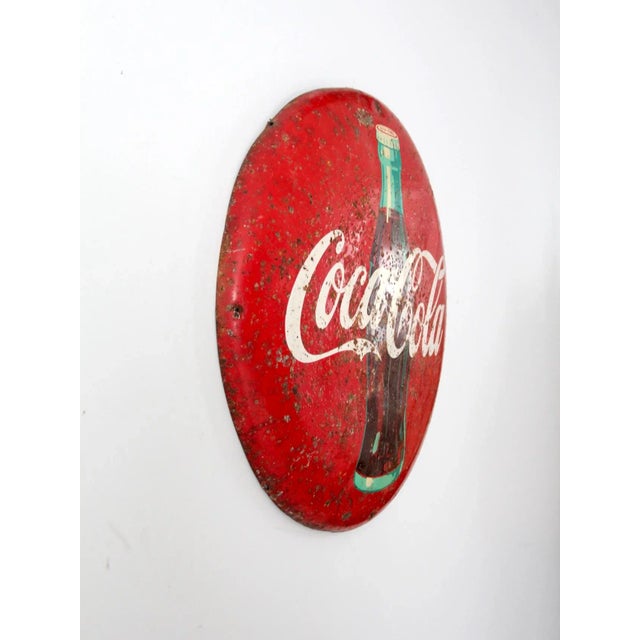 Vintage Coca-Cola sign dating to the 1950s, featuring the iconic bottle logo on a dimensional metal button sign....