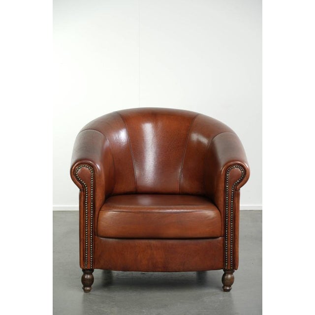 This sheepskin club armchair is crafted in a warm cognac color and finished with decorative nails. The armchair features a...
