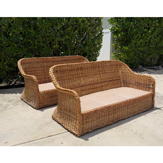A striking pair of vintage woven rattan lounge sofas featuring dramatic curved silhouettes and oversized braided trim....