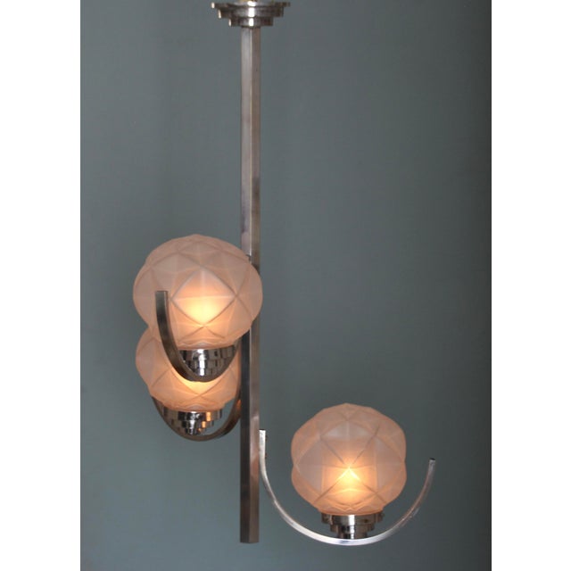 This Art Deco chandelier is chrome-plated and features three glass globes with Art Deco ornaments, offset in height. A...