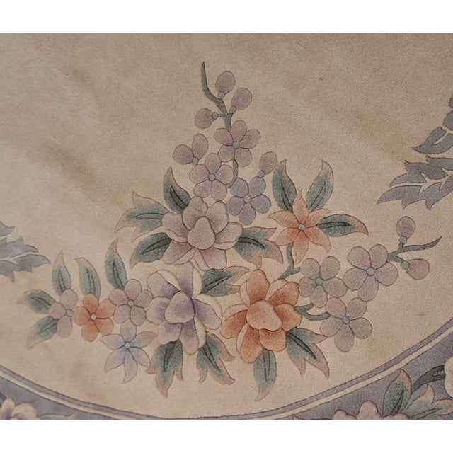 Round Chinese area rug featuring a soft ivory ground with an elaborate floral design in muted shades of dusty rose,...