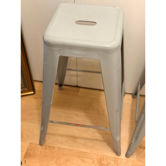 Set of three authentic Tolix Marais H65 counter-height stools in a soft grey-beige painted finish. An enduring French...
