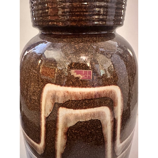 A tall, rounded ceramic vase with a ribbed collar neck, finished in a rich, speckled brown glaze that catches the light...