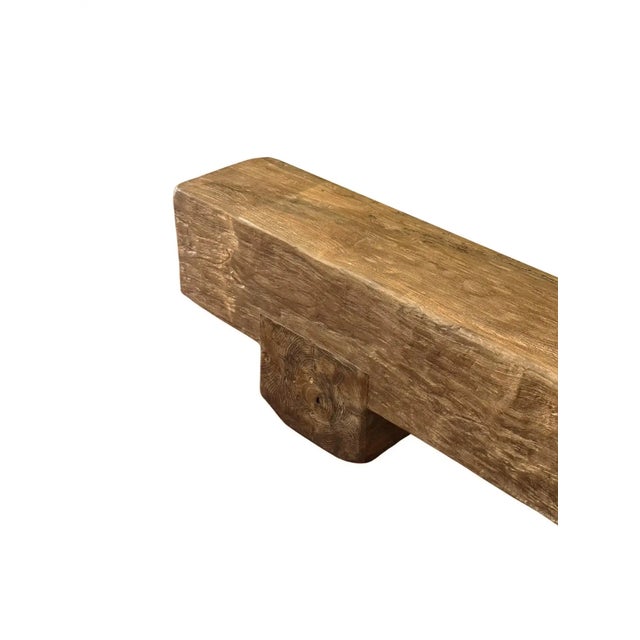 A sculptural bench crafted from solid teak wood, defined by its monolithic form and grounded proportions. The elongated...