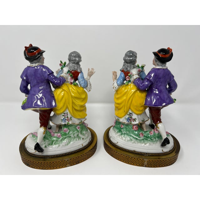A charming matched pair of Dresden-style porcelain courting couples, circa 1900, modeled in the Rococo revival taste with...