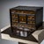Small wooden cabinet, black lacquered and gilt, with a fall-front opening. The interior comprises seven drawers with small...