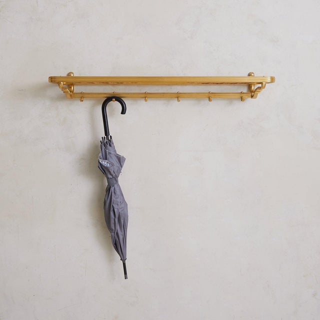 A 1960s Austrian wall-mounted coat rack, constructed in polished brass with a woven rope upper shelf. The elongated frame...