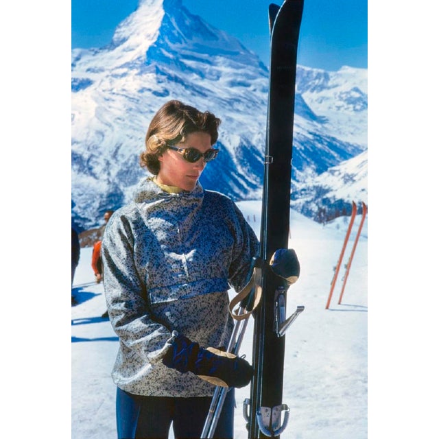 Shades and Skis by Toni Frissell A skier checks her skis before beginning the descent down a mountain in Zermatt,...