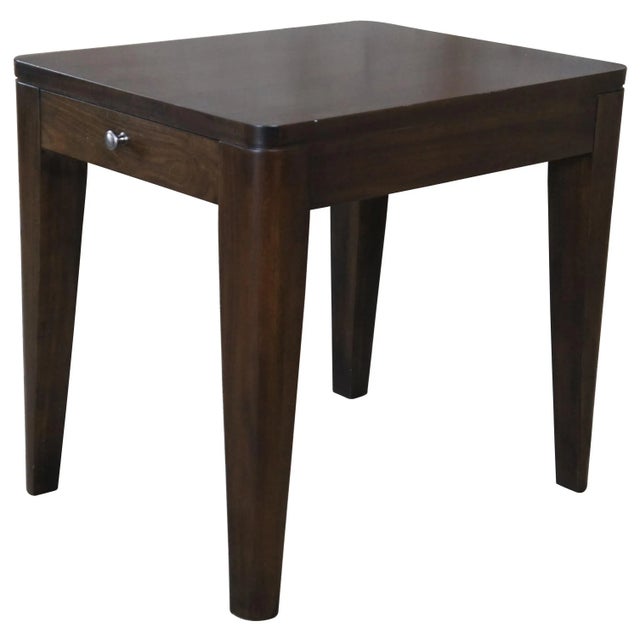 A modern end table by Heritage Home Group, 2017. A rectangular form finished in walnut with a central drawer featuring...