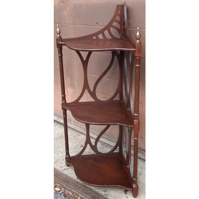 A Mid 20th Century three-tier mahogany corner display shelf featuring intricate carved fretwork and decorative brass...