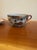 An elegant porcelain teacup and saucer set marked Nippon featuring traditional figural and landscape motifs in warm,...
