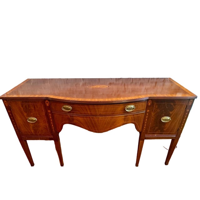 An elegant English mahogany sideboard in the refined Hepplewhite style, distinguished by delicate rosewood inlay work....