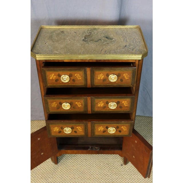 A marquetry side table with floral decoration. This small table opens with three drawers, and the lower section reveals a...