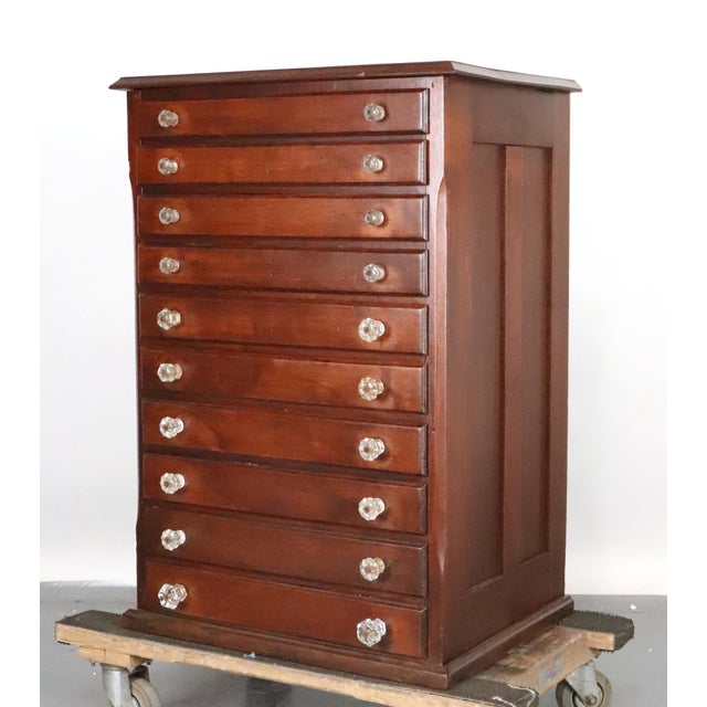 Antique optometrist's cabinet made of dark stained walnut with clear glass knobs. Patented Geneva. It features ten...