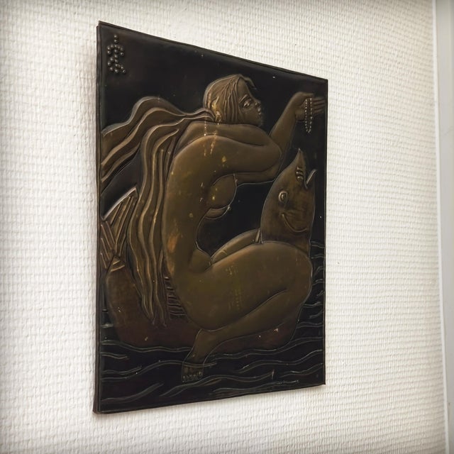 Repoussé brass plaque depicting a woman riding a dolphin. Highly detailed brasswork from the 1960s, mounted on a wooden...