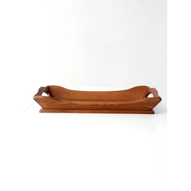 This vintage carved wood tray features a long rectangular form with curved handles and raised sides for easy carrying. The...