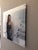 This artwork features a figure in a strapless blue gown, set against a backdrop of soft clouds and water, creating a...