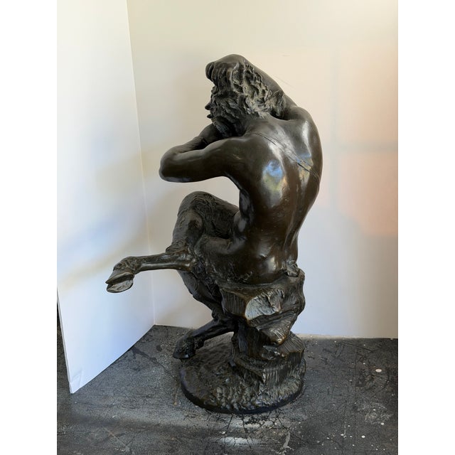 A large-scale patinated bronze depicting a bearded satyr seated on a naturalistic rocky base, head thrown back with one...