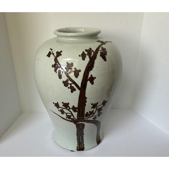 A large hand-painted porcelain jar. Featuring a striking, earthy "rusty brown" twisted tree and weeping plum motif, the...