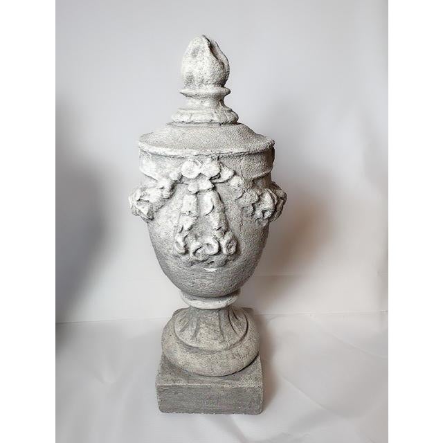 Stunning pair of cast concrete neoclassical urns adorned with floral garlands and floral final and round fluted base. A...