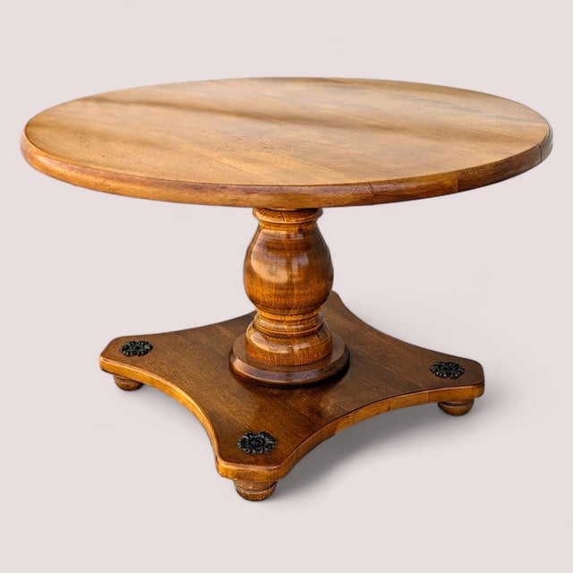 A vintage round solid-maple pedestal table with a turned central column, a shaped quadriform base, and four dark...
