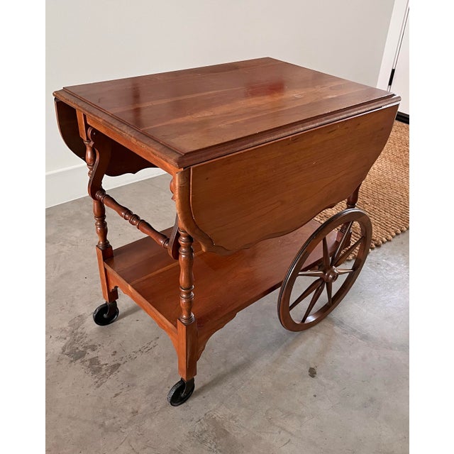 A beautifully crafted mid-century beauty featuring drop-leaf sides, wooden back wheels, and a two-tiered lower storage...