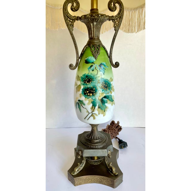 Here is a charming, antique Victorian Revival table lamp featuring a hand-painted floral glass body, ornate cast metal...