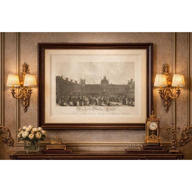 This impressive early 19th-century engraving depicts the Cour Carrée of the Louvre Palace in Paris during the historic...