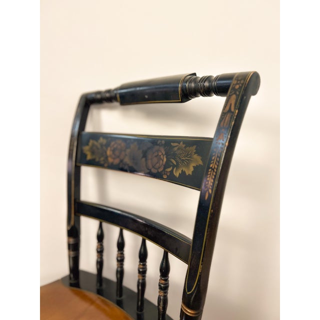 Classic Hitchcock chair featuring a deep black finish with traditional gold stenciled detailing and turned spindle back....