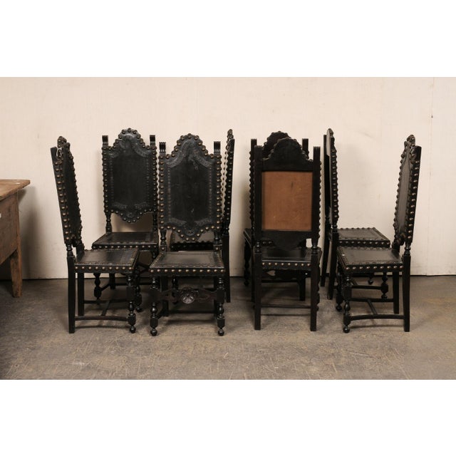 A Spanish set of eight carved wood and tooled leather side chairs from the mid 20th century. These vintage chairs from...