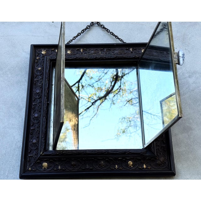 This charming antique triptych wall mirror cabinet features three folding glass panels set within an ornate dark wooden...