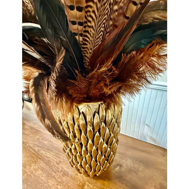 This striking decorative arrangement composed of primarily natural pheasant feathers, presented in a distinctive golden,...