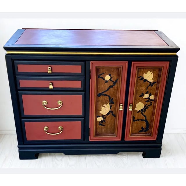 This Asian style server is finished in an oxblood red with black and gold embellishments. The two doors feature stylized...