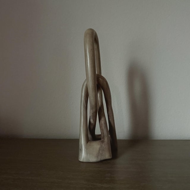 A sculptural hand carved soapstone love knot featuring intertwined looping forms and a softly polished finish. Natural...