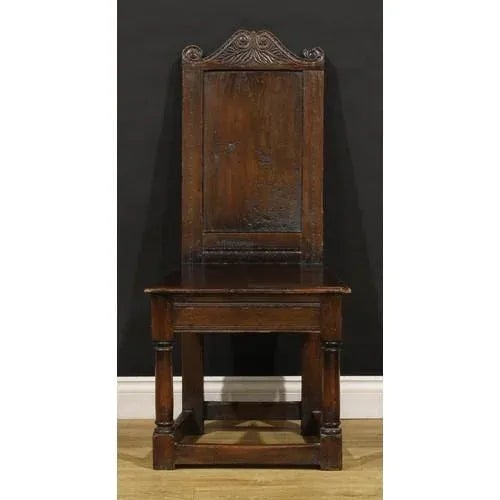 A pair of 18th century English oak panel back side or hall chairs, each shaped cresting rail carved with leafy scrolls,...