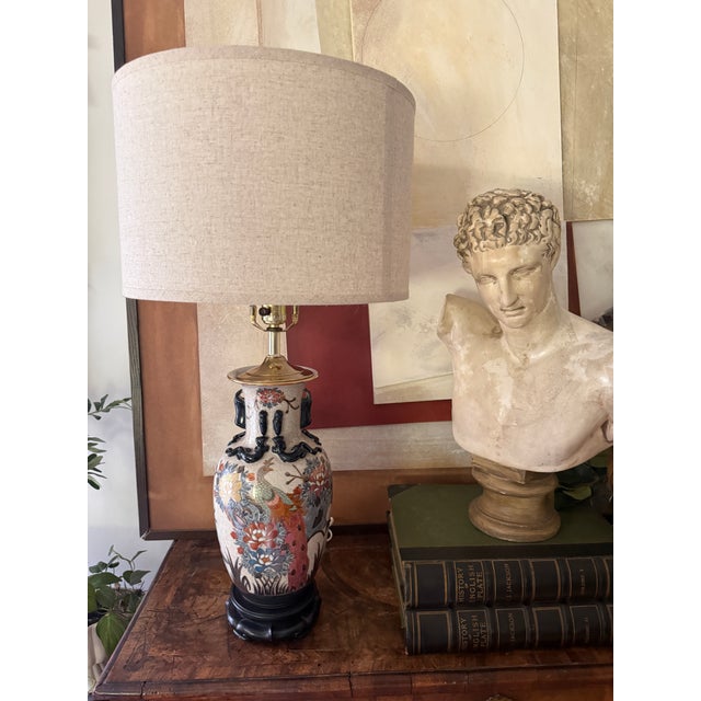 A richly detailed vintage Asian-inspired ceramic table lamp featuring an elegant peacock amid lush floral motifs. The...