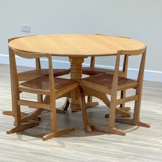 A refined mid-century dining set comprising a circular elm table and four matching rattan chairs, preserved in its...
