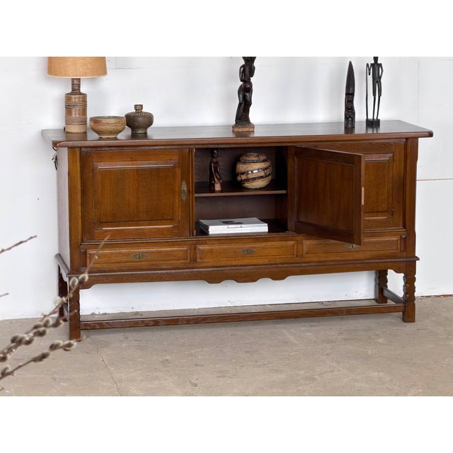 Danish sideboard in dark stained oak by Henning Kjærnulf, dating from the 1960s. Its broad, low-set cabinet, carved legs...