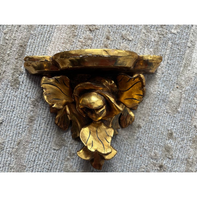 A beautifully carved wooden pair of gessoed and gilt wall brackets, the overhanging shelves above carved roses with leaf...