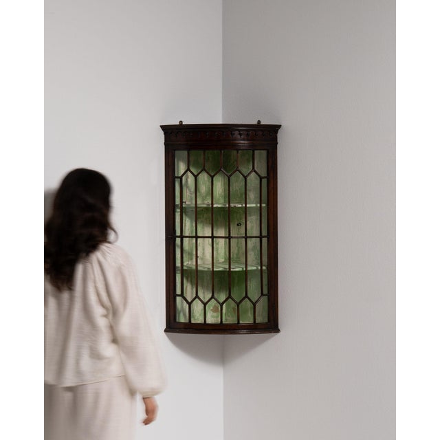 This corner display cabinet makes its impression through dark mahogany, leaded glass doors. Dating to 19th Century and...