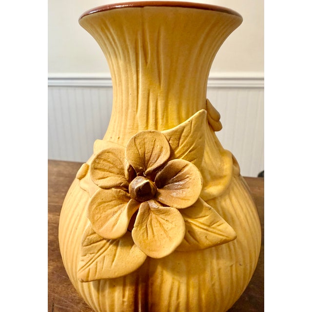 This vase is characterized by its rich mustard yellow/tan body with a prominent ribbed texture, accented by darker brown...