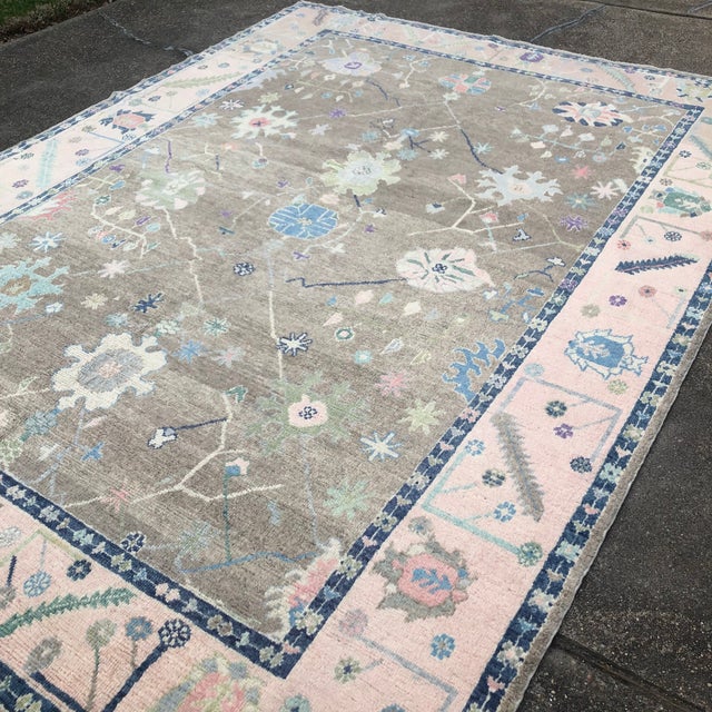 A refined Turkish Oushak rug featuring a warm Makara brown field framed by a soft pink border, with large-scale floral...