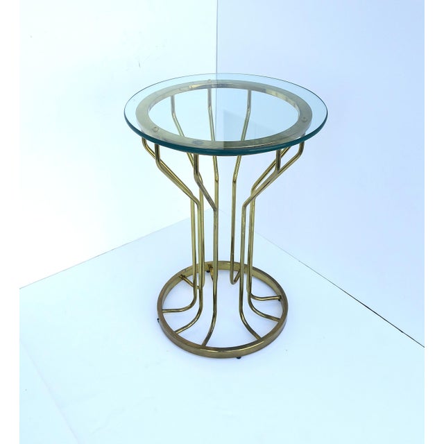 A brass‑plated hourglass‑form side table with glass top, in the style of Modern and Postmodern design styles, circa...
