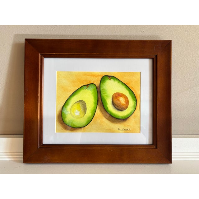This vibrant, original watercolor painting captures the beauty and fresh appeal of a sliced avocado, showcasing its vivid...