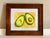 This vibrant, original watercolor painting captures the beauty and fresh appeal of a sliced avocado, showcasing its vivid...