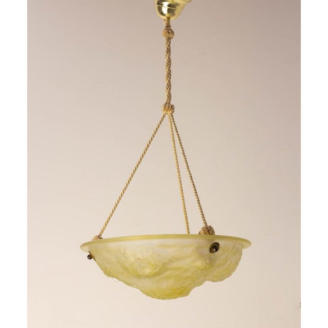 An elegant hanging chandelier featuring a bowl made of molded and pressed glass, slightly opalescent, in a delicate pale...