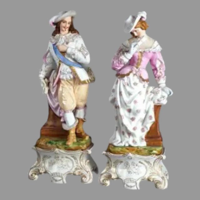 An antique pair of French porcelain figurine statues of a courting couple, hand painted in pastel colors and gilt...