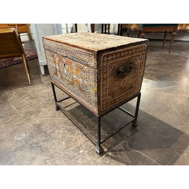 The Antique Syrian Bone Inlaid Chest on Iron Base is a decorative furniture piece that adds a touch of charm to any room....