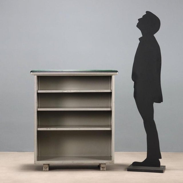 Bookcase with adjustable shelves, enamelled metal, top covered in skai and transparent glass on top. This piece is...